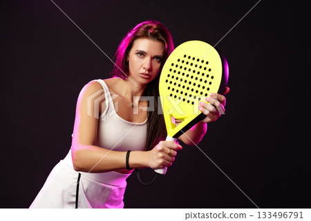 Female athlete posing with a bright yellow paddle racket in a dark studio setting 133496791