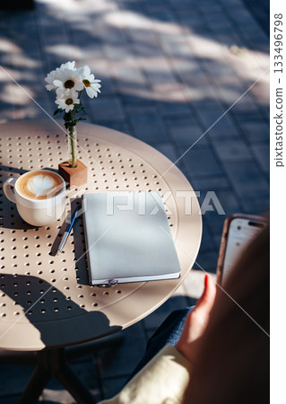 Cozy coffee table with latte, notebook and flowers in a sunny outdoor setting 133496798