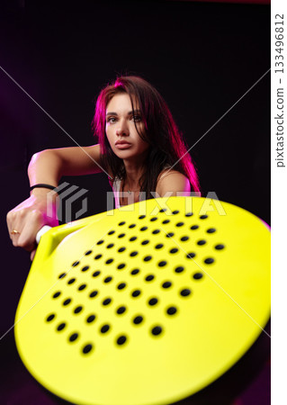Young woman holding a yellow paddle amidst colorful lighting in a studio space 133496812