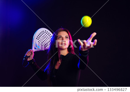 Young woman preparing to serve a tennis ball in a vibrant indoor setting 133496827