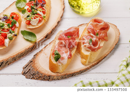 Tasty antipasto toasts featuring classic caprese with mozzarella and tomatoes, and savory prosciutto with herbs Tasty antipasto toasts featuring classic caprese with mozzarella and tomatoes, and savory prosciutto with herbs 133497508