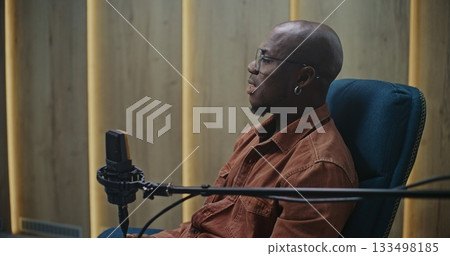 Expert Speaker With Glasses and Earring, Positioned Professional Microphone in Modern Audio Studio Expert Speaker With Glasses and Earring, Positioned Professional Microphone in Modern Audio Studio 133498185