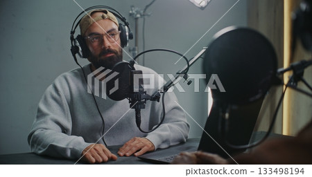 Podcast Host With Open Laptop Listening to Guest, Both Using Headphones and High End Microphones Podcast Host With Open Laptop Listening to Guest, Both Using Headphones and High End Microphones 133498194