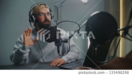 Podcast Host With Open Laptop Listening to Guest, Both Using Headphones and High End Microphones Podcast Host With Open Laptop Listening to Guest, Both Using Headphones and High End Microphones 133498298