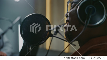 Man in Glasses and Headphones Speaking Emotionally Into Professional Studio Microphone Man in Glasses and Headphones Speaking Emotionally Into Professional Studio Microphone 133498515