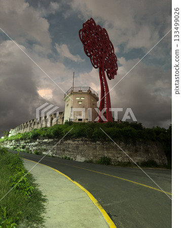 Old fortress with a large red tree sculpture under cloudy sky 133499026