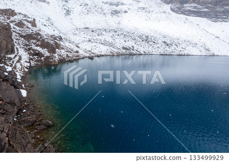 Snow-covered rocks and blue water on the lakeside 133499929