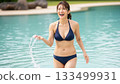 A woman in a bikini scooping water from a pool and laughing happily 133499931