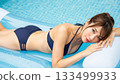 A woman in a swimsuit smiling while lying on an air mattress above the water in a pool 133499933