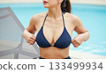 A woman adjusts her bikini top by the pool 133499934