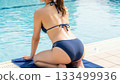 Back view and hips of a woman in a bikini sitting by the pool 133499936