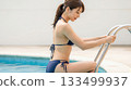 A woman in a bikini lying by the pool with her legs raised and smiling 133499937