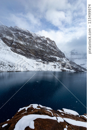 Snow-covered rocks and azure lake_vertical 133499974