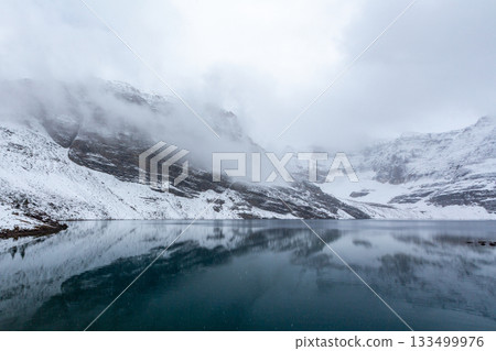 白雪皚皚的山峰和低垂的雲朵倒映在湖面上。 133499976