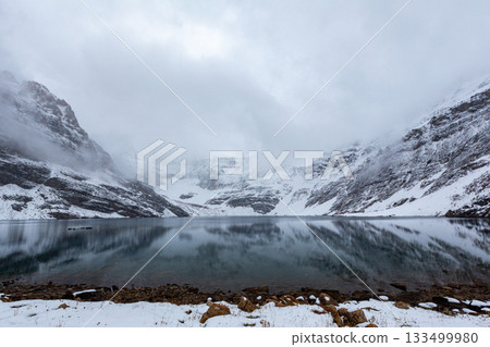 陰天里白雪皚皚的山峰倒映在深湖中。 133499980