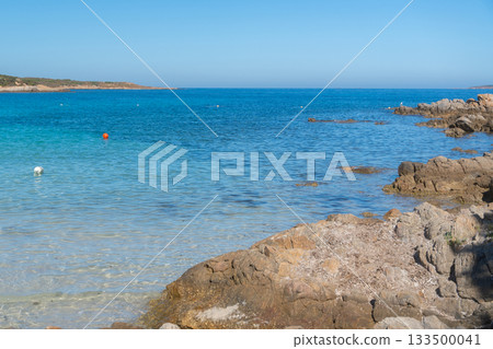 Turquoise coastal water meets rugged shoreline rocks under a bright summer sky, Sardinian, La Maddalena, Italy 133500041