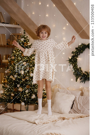 Caucasian child jumping on bed in cozy bedroom with Christmas tree and white wall 133500408