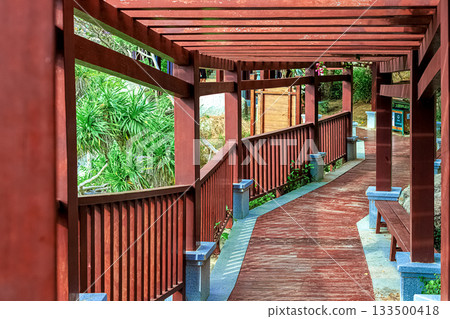 A covered wooden path in a green park, stretching into the distance. China, Hainan Sky Grottoes Park 133500418
