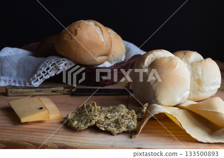 Fresh baked bread rolls in a rustic basket and on a wood table, pairing with sliced smoked cheese with pepper. Perfect for cooking magazines Fresh baked bread rolls in a rustic basket and on a wood table, pairing with sliced smoked cheese with pepper. Perfect for cooking magazines 133500893