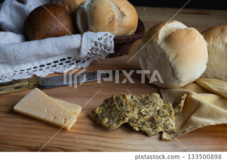 Assortment of baked bread rolls including wholemeal and rustic white, fresh cheese slices, and multigrain crackers Assortment of baked bread rolls including wholemeal and rustic white, fresh cheese slices, and multigrain crackers 133500898