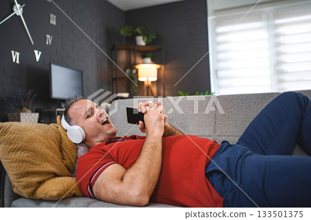 Happy man singing while listening music on the headphonesat home 133501375