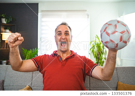 Excited middle aged man watching soccer game at home Excited middle aged man watching soccer game at home 133501376