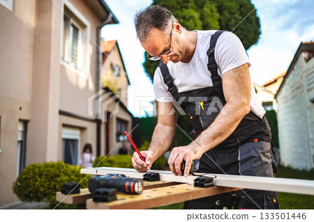 Mature male carpenter measuring wooden plank outdoors 133501446