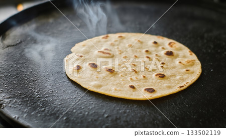 Freshly cooked flatbread on hot griddle with steam rising above 133502119