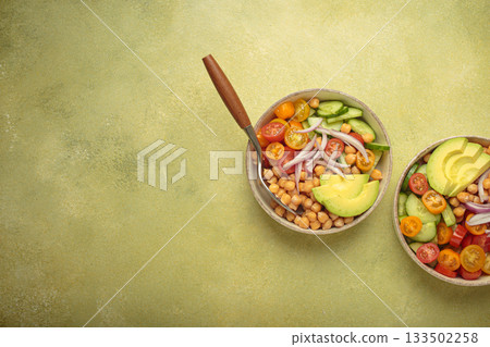 Two bowls with vibrant vegetarian chickpea salad with fresh vegetables in ceramic bowls top view on light green background, space for text 133502258