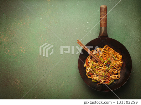 Asian style stir fry noodles with chicken and vegetables in a black wok pan with chopsticks, space for text 133502259