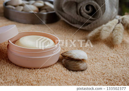 Open container of nourishing moisturizing cream for skincare routine during a relaxing spa and wellness treatment with seashells and soft towels, promoting beauty and self care 133502377