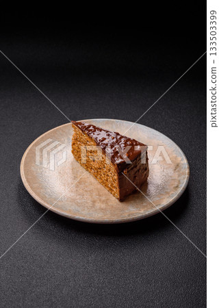 A slice of sweet layered cake covered in chocolate with nuts and caramel. A slice of chocolate cake 133503399