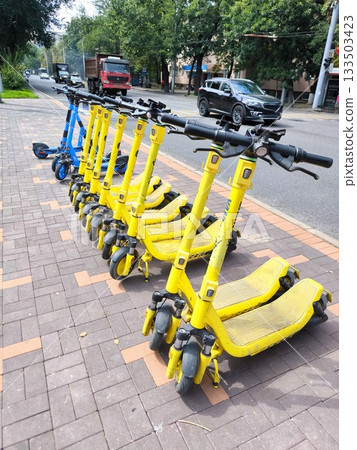 A row of yellow electric scooters on a city street A row of yellow electric scooters on a city street 133503423