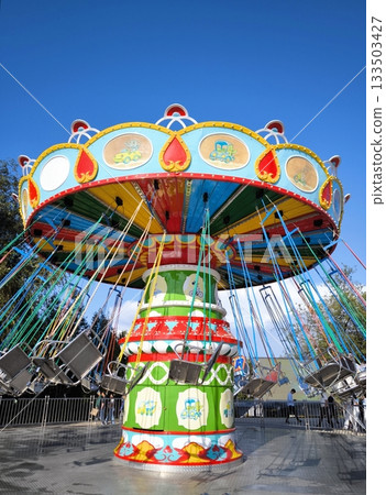 A brightly colored chain carousel in an amusement park against a blue sky A brightly colored chain carousel in an amusement park against a blue sky 133503427