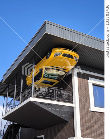 A yellow car attached to the ceiling of a balcony of a building that simulates an upside-down house 133503436