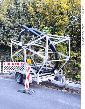 A trailer with a spool of large diameter black plastic pipes for laying communications 133503458
