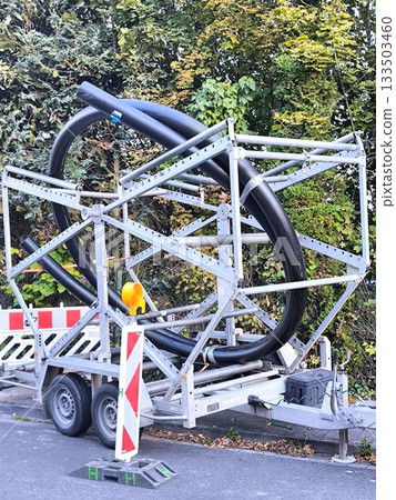 A trailer with a spool of large diameter black plastic pipes for laying communications 133503460