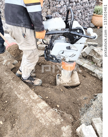 A worker compacts the soil with a vibrating plate 133503461