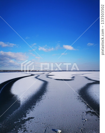 A freezing lake. A polynya, thin ice on a frozen or snow-covered landscape under a blue sky. 133503502