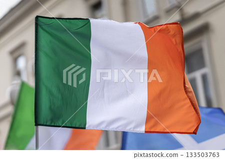 Saint Patrick day holiday. Irish tricolor flag green white orange waves in breeze above city parade crowd. St. Patrick Day national celebration 133503763