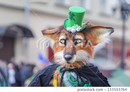 Participant in the St. Patrick's Day Parade. Person in fox mask costume and green top hat standing among people crowd outdoors. Creative masquerade, quirky holiday costume 133503764