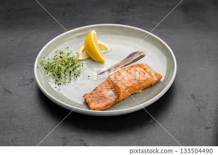 Grilled salmon fillet with lemon and microgreens on plate, gourmet restaurant plating 133504490