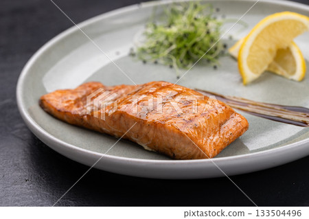 Grilled salmon fillet with lemon and microgreens on plate, gourmet restaurant plating 133504496