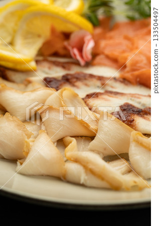 Close up of smoked fish slices with lemon garnish on plate, seafood appetizer macro Close up of smoked fish slices with lemon garnish on plate, seafood appetizer macro 133504497