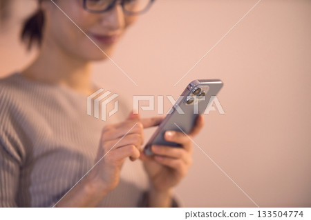 A middle-aged woman relaxing in the living room and looking at her smartphone A middle-aged woman relaxing in the living room and looking at her smartphone 133504774