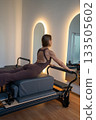 Woman doing Swan exercise on Pilates Reformer for the chest and back muscles, focusing on flexibility, strength, and control with determination 133505602