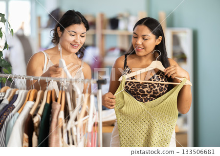 Two young women choosing summer dresses or tops in clothing store Two young women choosing summer dresses or tops in clothing store 133506681