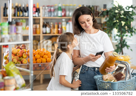 Girl with mother customers at shop scans QR code on juice package using phone camera Girl with mother customers at shop scans QR code on juice package using phone camera 133506782