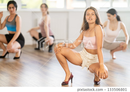 Girls perform dance in heels, squat down, actively repeat movements of instructor. Girls perform dance in heels, squat down, actively repeat movements of instructor. 133506801