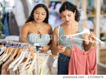 Two young women choosing summer dresses or tops in clothing store Two young women choosing summer dresses or tops in clothing store 133506876
